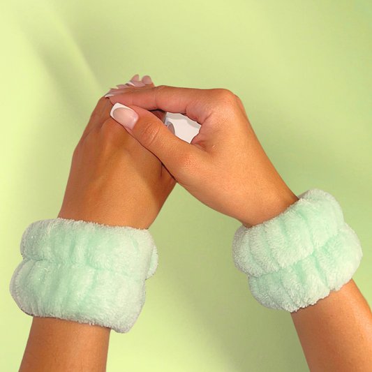 Hands wearing light green fuzzy spa wristbands against a light green background